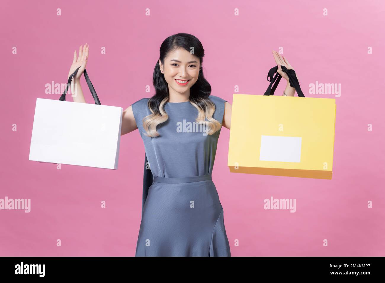 Asian happy female woman girl holds colourful shopping packages standing on pink background Stock Photo