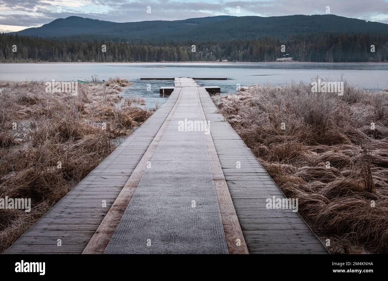 Wooden pier on lake site facing a beautiful mountain on a misty winter morning. Cold winters morning on a forest lake. Frosty calm landscape. Natural Stock Photo