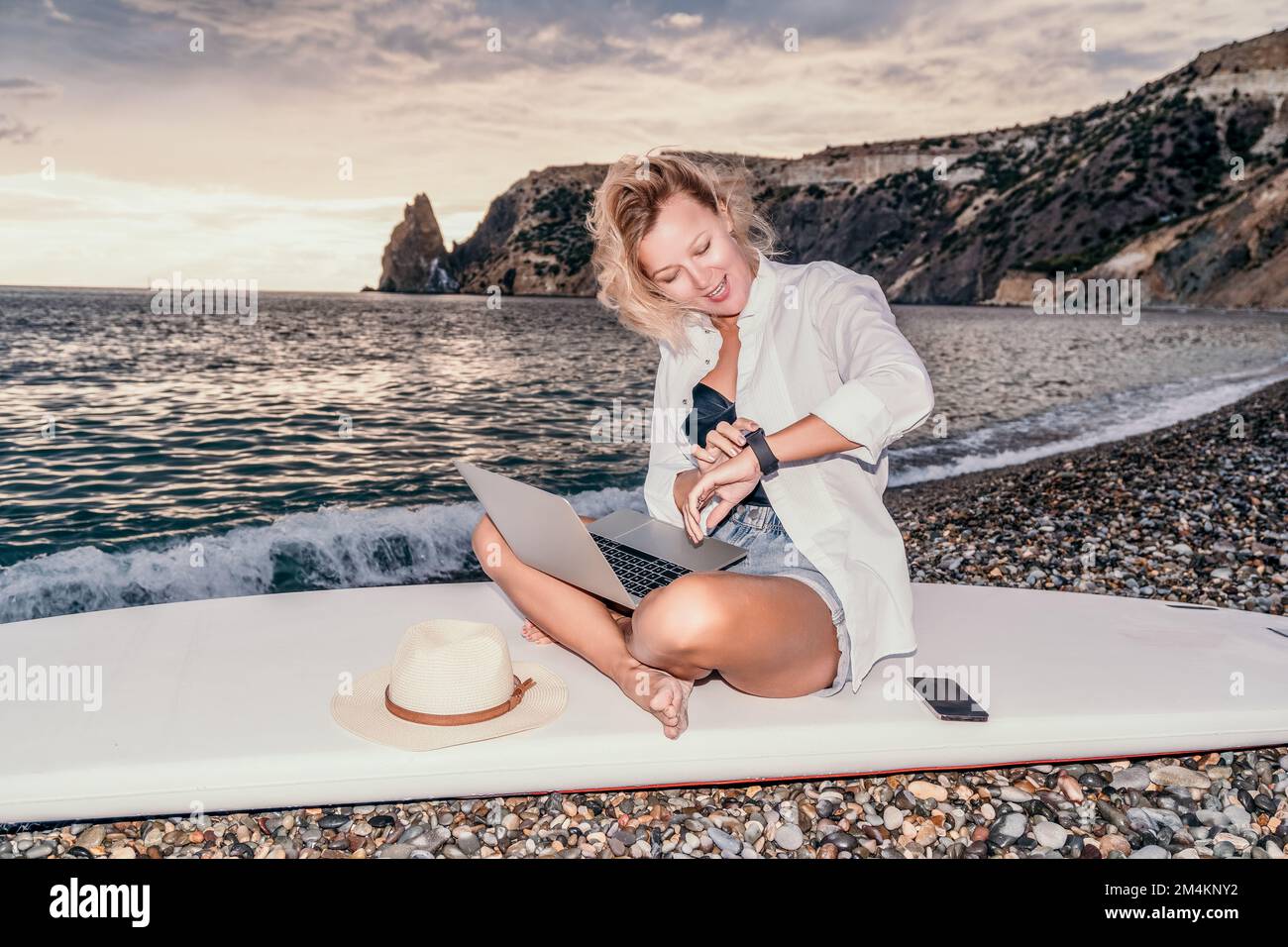 Digital nomad, Business woman working on laptop by the sea. Pretty lady typing on computer by the sea at sunset, makes a business transaction online Stock Photo