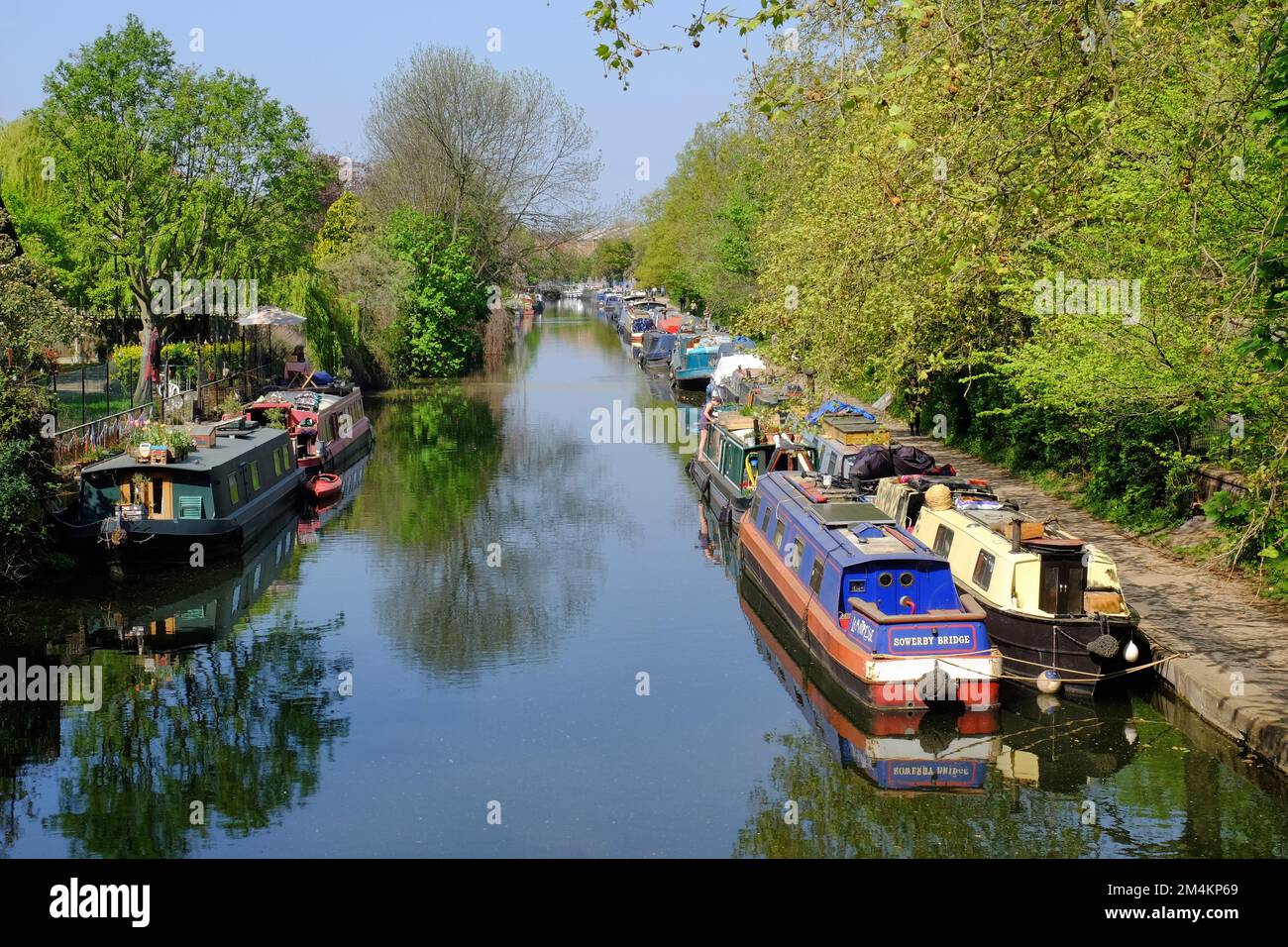 Colourful barges (houseboats) moored and reflections and trees along Regent’s Canal at Victoria Park, London, England Stock Photo