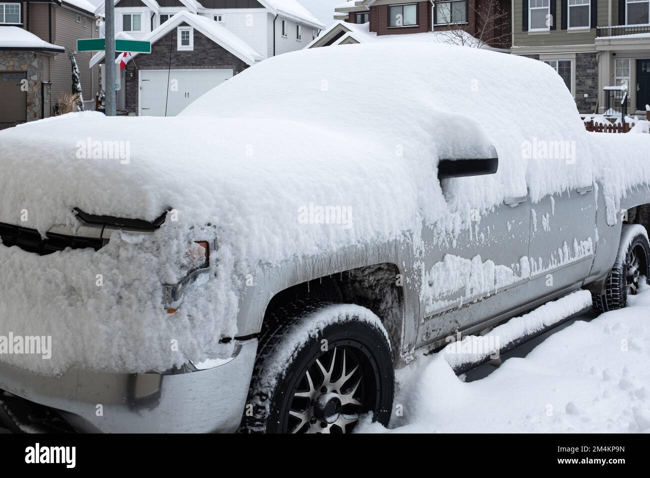 A car under the snow. Winter urban scene in Canada. Vehicles covered with snow in the winter blizzard in the parking. Cars in snowdrifts after a snowf Stock Photo