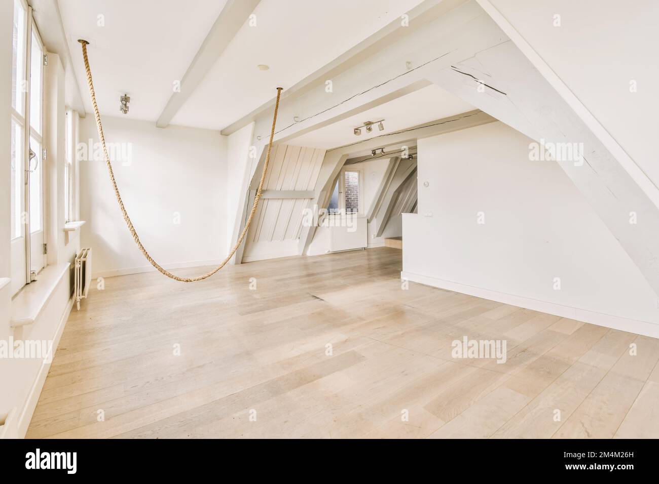 an empty room with white walls and wood flooring on one side, there is a rope hanging from the ceiling to the other Stock Photo