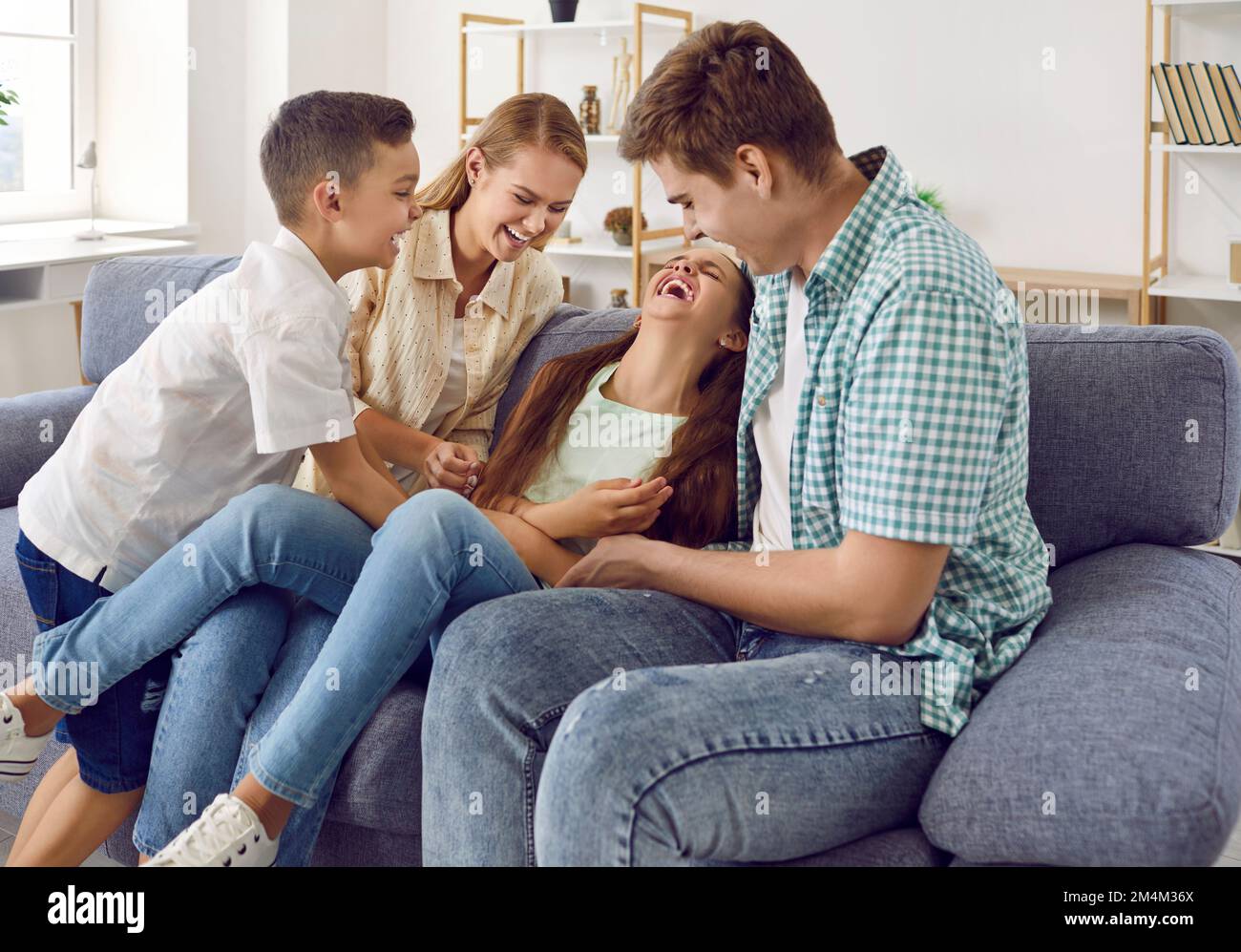 Happy family are playing together, they tickling a girl sitting on couch and laugh in living room. Stock Photo
