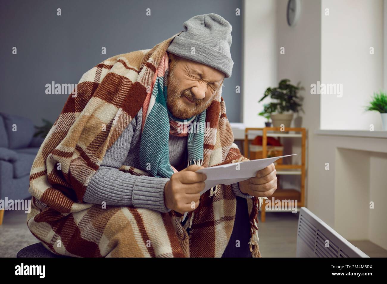 Sad poor senior man feeling cold at home, holding heating or electricity bill and crying Stock Photo