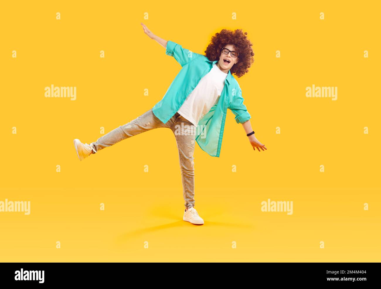 Happy, cheerful, funny boy in red curly wig, dressed in casual clothes, fooling around and dancing Stock Photo