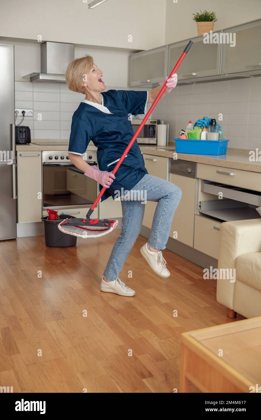 Housewife or cleaning lady in protective apron and gloves dancing in