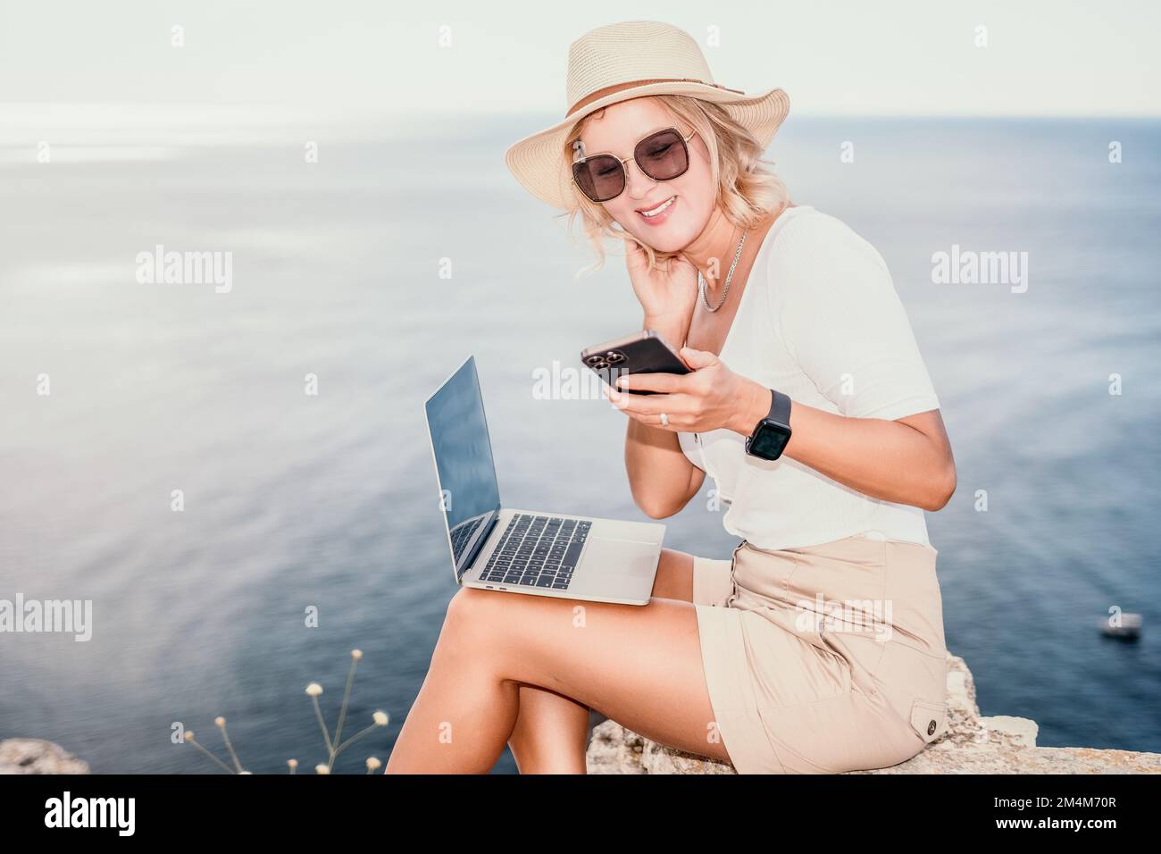 Digital nomad, Business woman working on laptop by the sea. Pretty lady typing on computer by the sea at sunset, makes a business transaction online Stock Photo