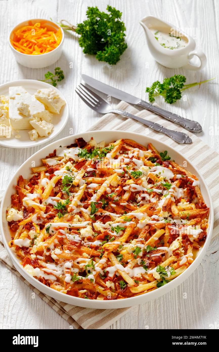 Bacon Mozzarella Feta Cheddar Cheese Fries with ranch dressing and parsley on white dish on wood table with ingredients, american cuisine, vertical vi Stock Photo