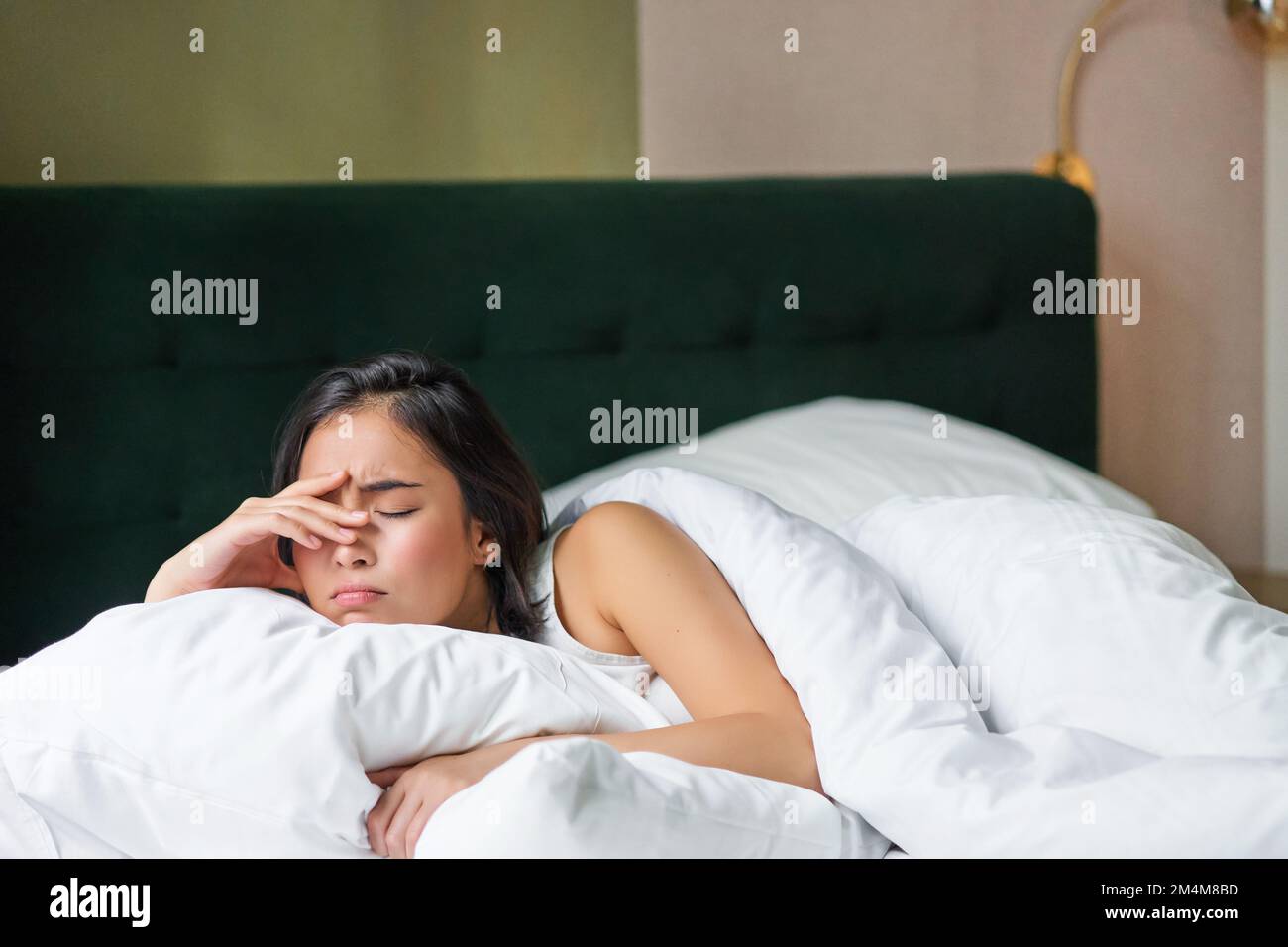 Sad and distressed young korean woman lying in her bed with pillow and ...