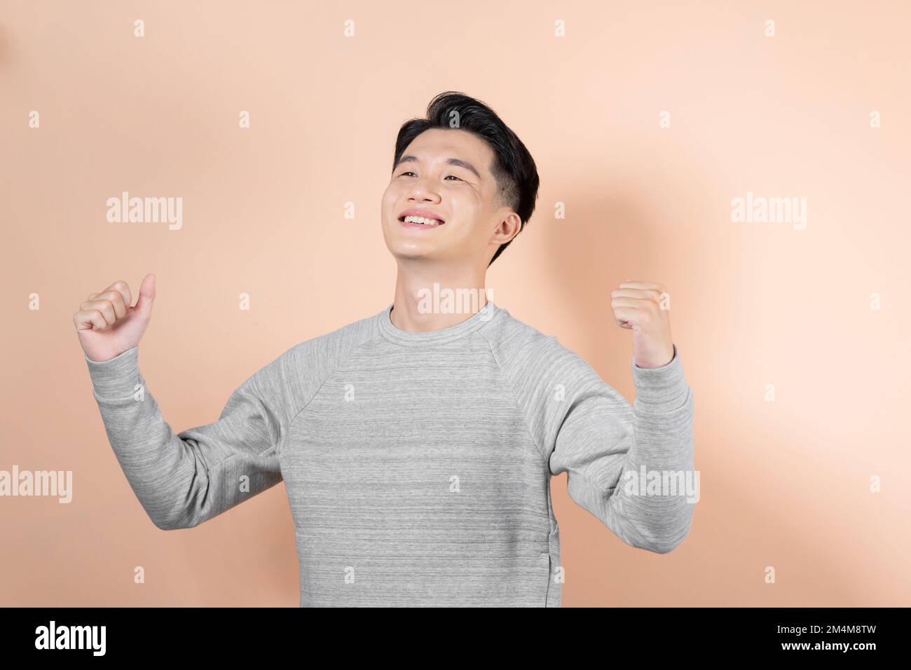 Excited young Asian man celebrating success with raised fist isolated on beige background. Stock Photo