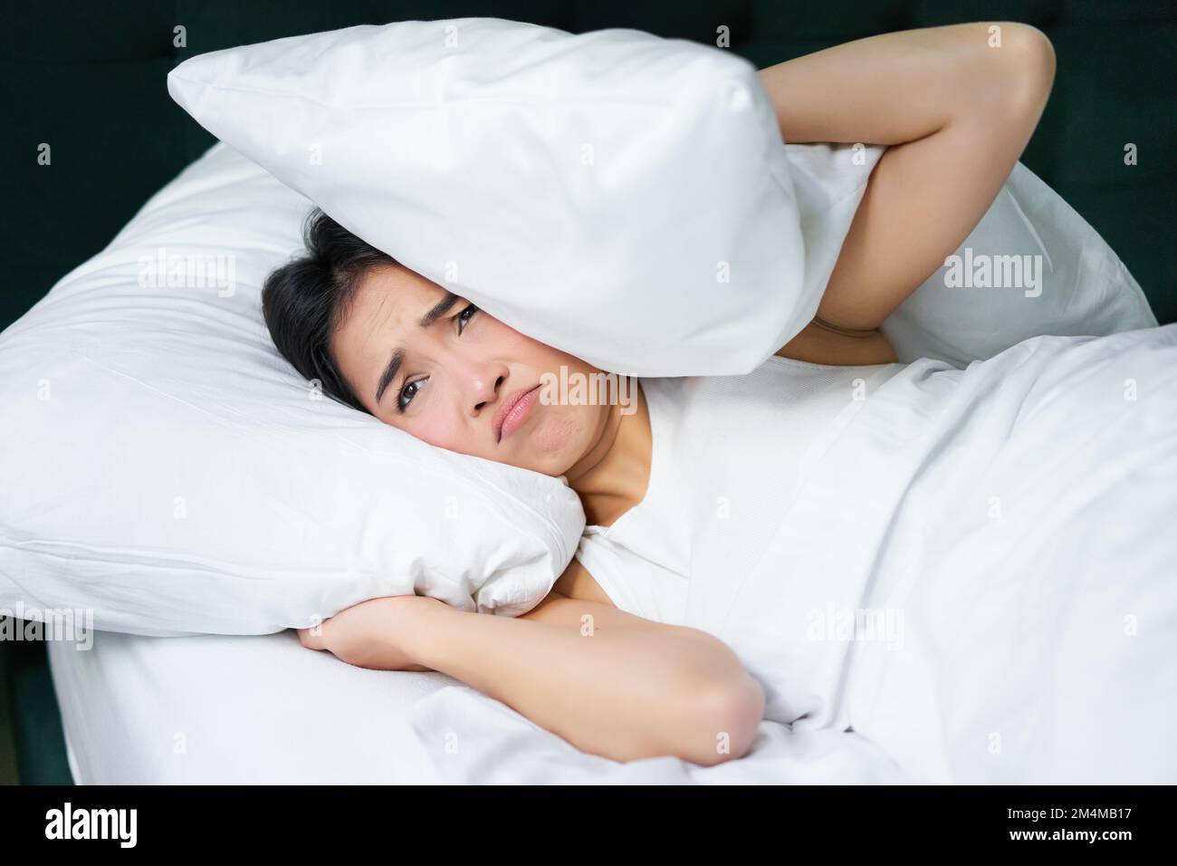 Sad girl with insomnia. Young asian woman lying in bed, cover her ears