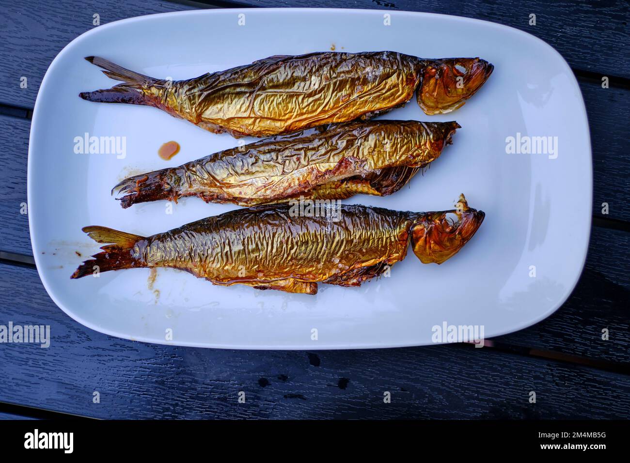 Three bucklings, freshly smoked herring, on a white serving platter, as so-called "golden Bornholmers" a specialty on the island of Bornholm, Denmark. Stock Photo