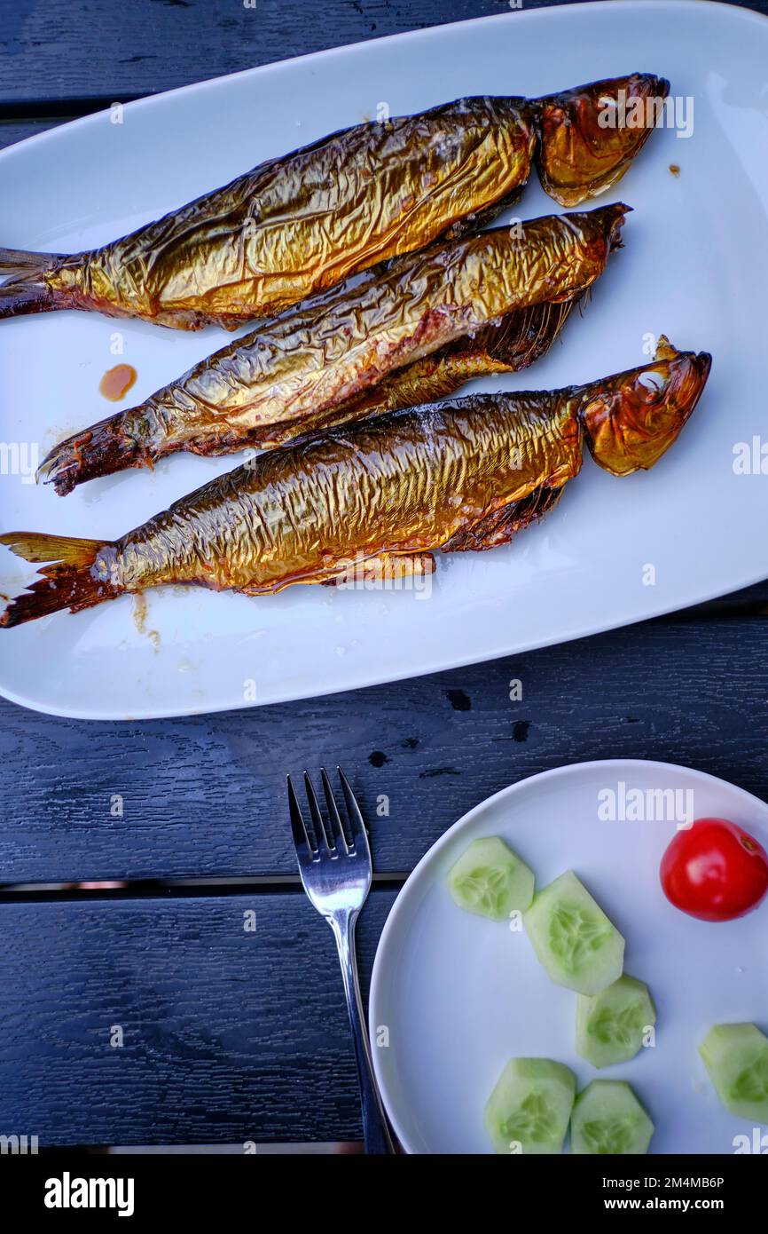 Three bucklings, freshly smoked herring, on a white serving platter, as so-called "golden Bornholmers" a specialty on the island of Bornholm, Denmark. Stock Photo
