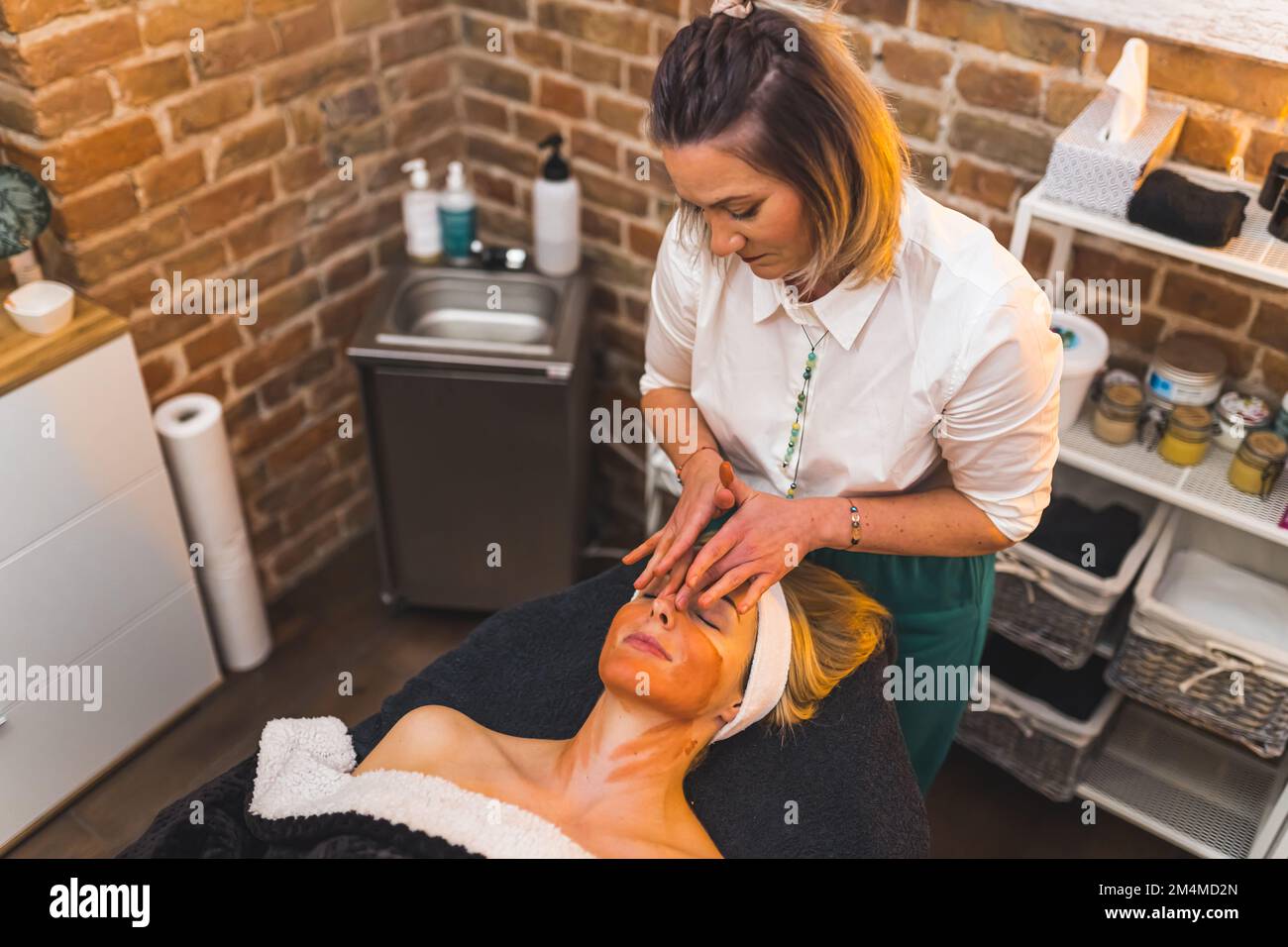 Rejuvenating face massage and orange clay face mask. High angle view of facial procedure at SPA facility. Two women. High quality photo Stock Photo