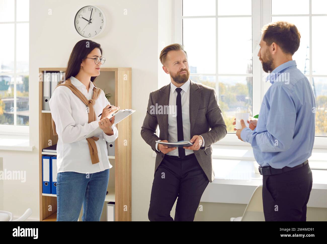 Two businessmen and female trainee or secretary are discussing work tasks together in office. Stock Photo