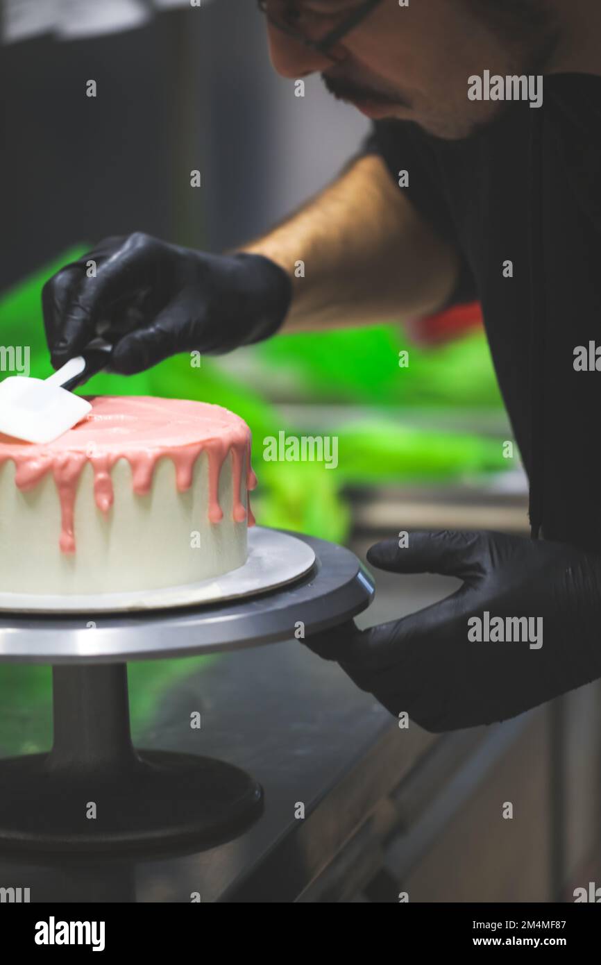 cake chef designer using spatula to smooth and level pink dripping on