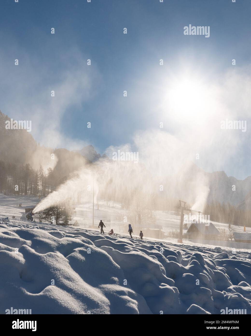 Family sledding under Snowmaking machine snow cannon in action on a cold sunny winter day in ski resort Stock Photo