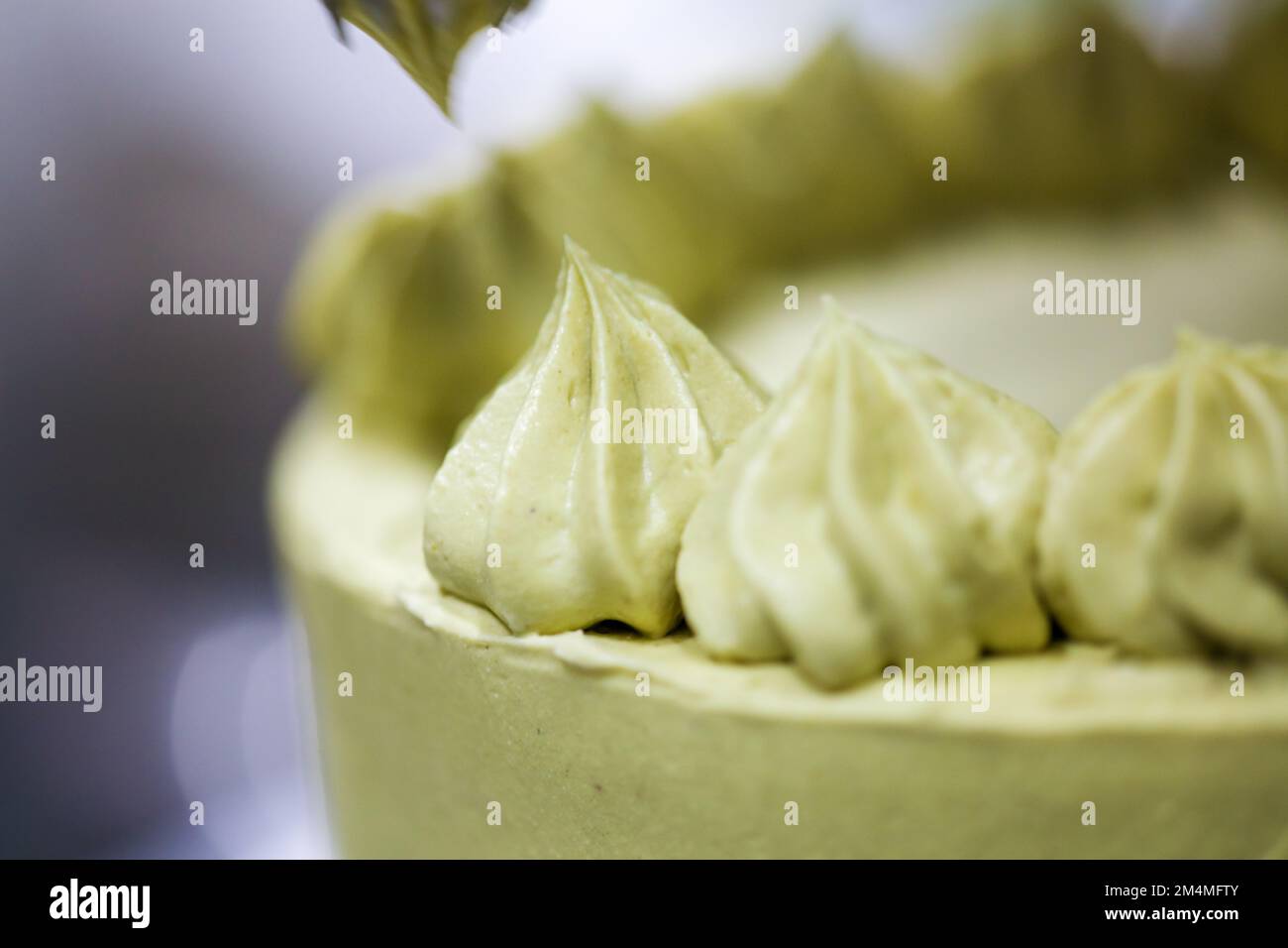 pastry chef designer making swirls with piping bag pistachio cream filling on layered green frosted chocolate cake Stock Photo