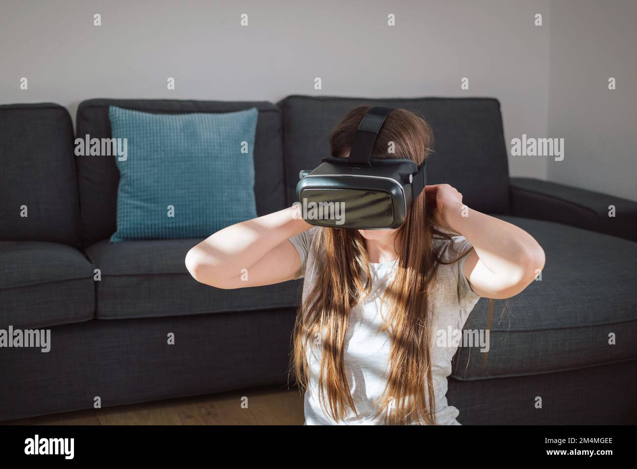 Young woman immersing in the virtual world using a VR headset while sitting in the cozy living room Stock Photo