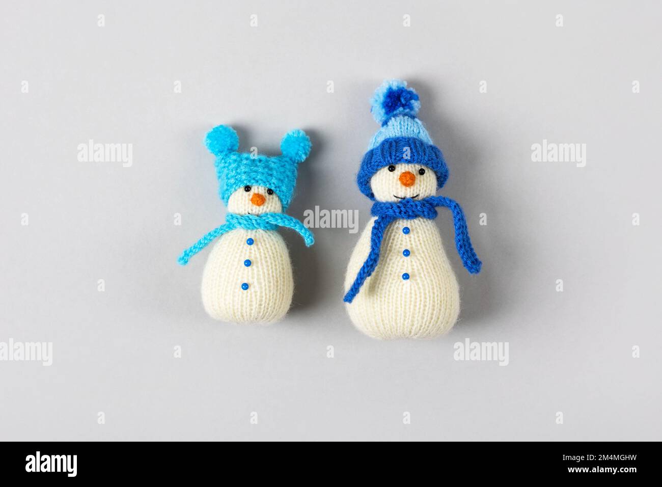Two funny knitted snowmen in blue hats and scarves on a gray background. Merry Christmas and New Year 2023 greeting card Stock Photo