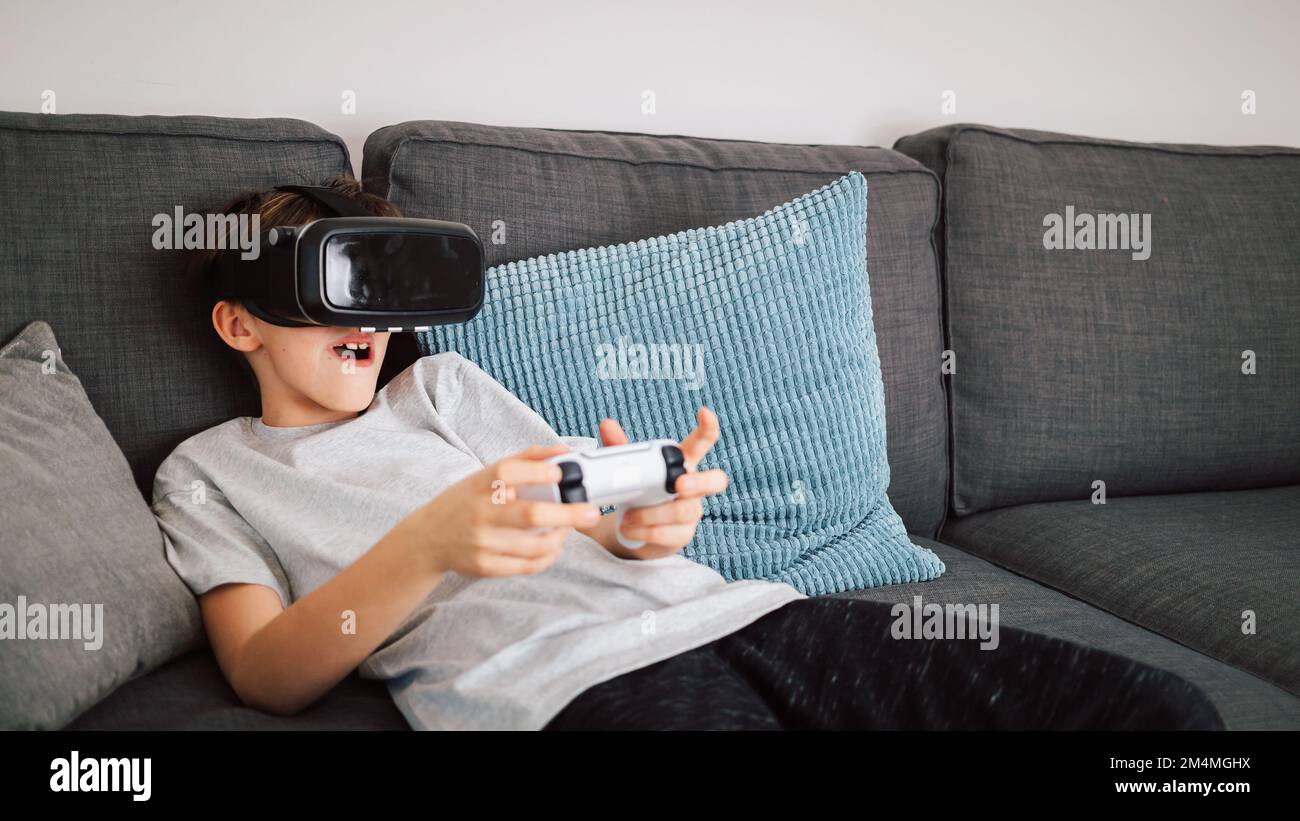 Caucasian boy enjoying at home, gaming using VR box, virtual reality goggles, and simulator, moving and physically interacting with a virtual world Stock Photo