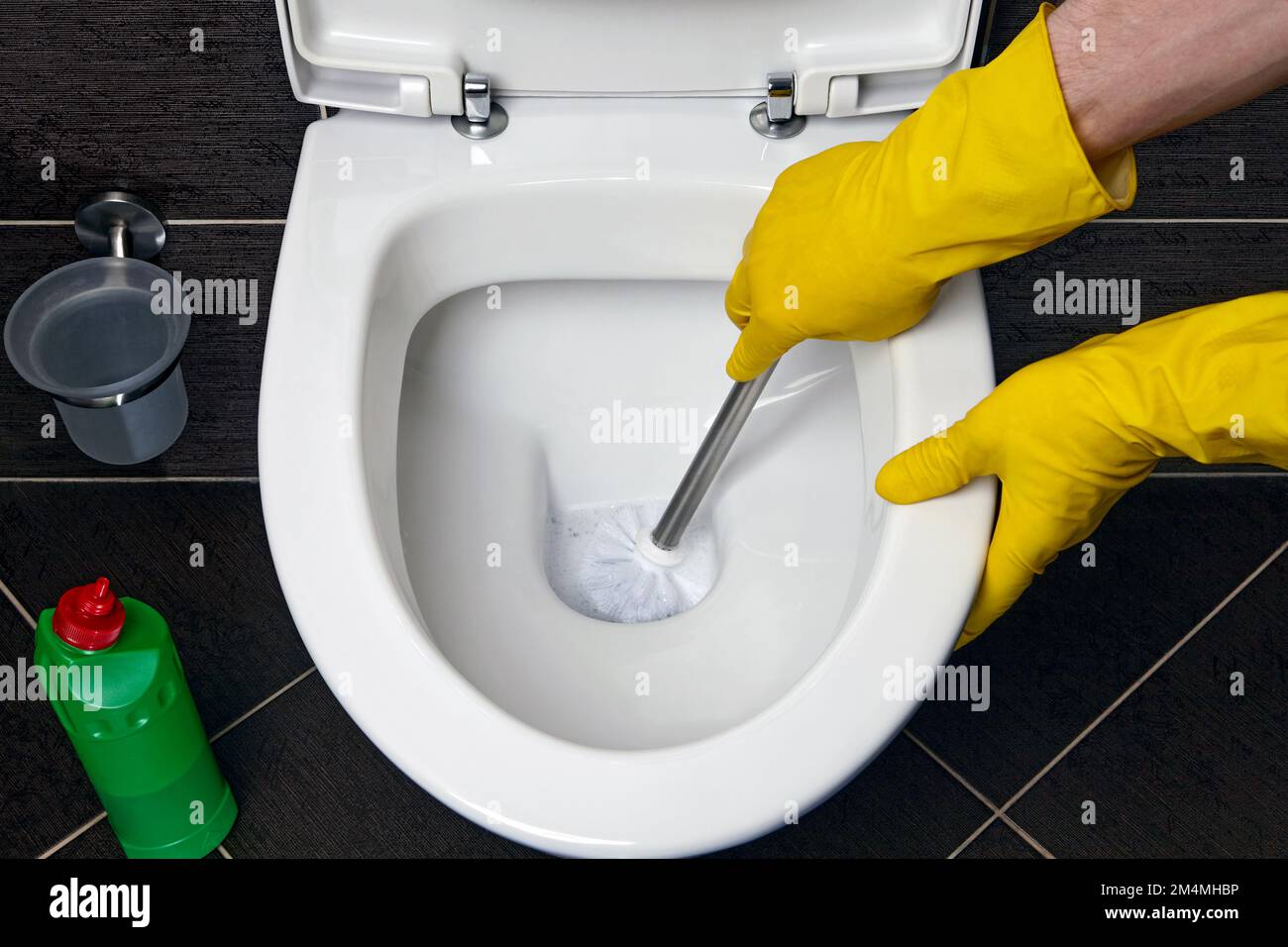 A man in yellow rubber gloves cleans the toilet bowl with a brush and
