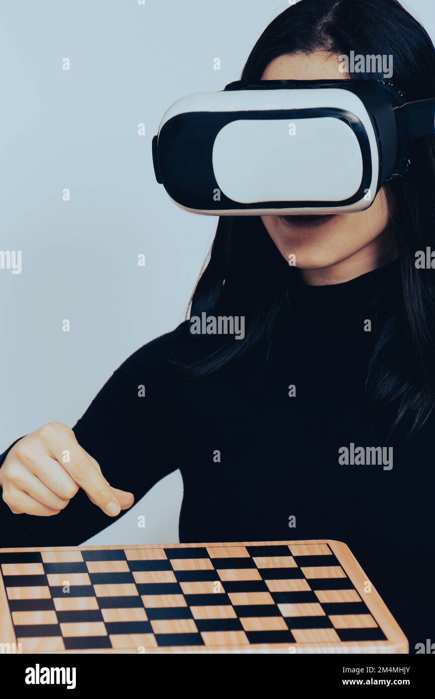 Close up portrait excited caucasian woman wear VR set and play chess in isolated background. Virtual reality games and metaverse experience concept Stock Photo