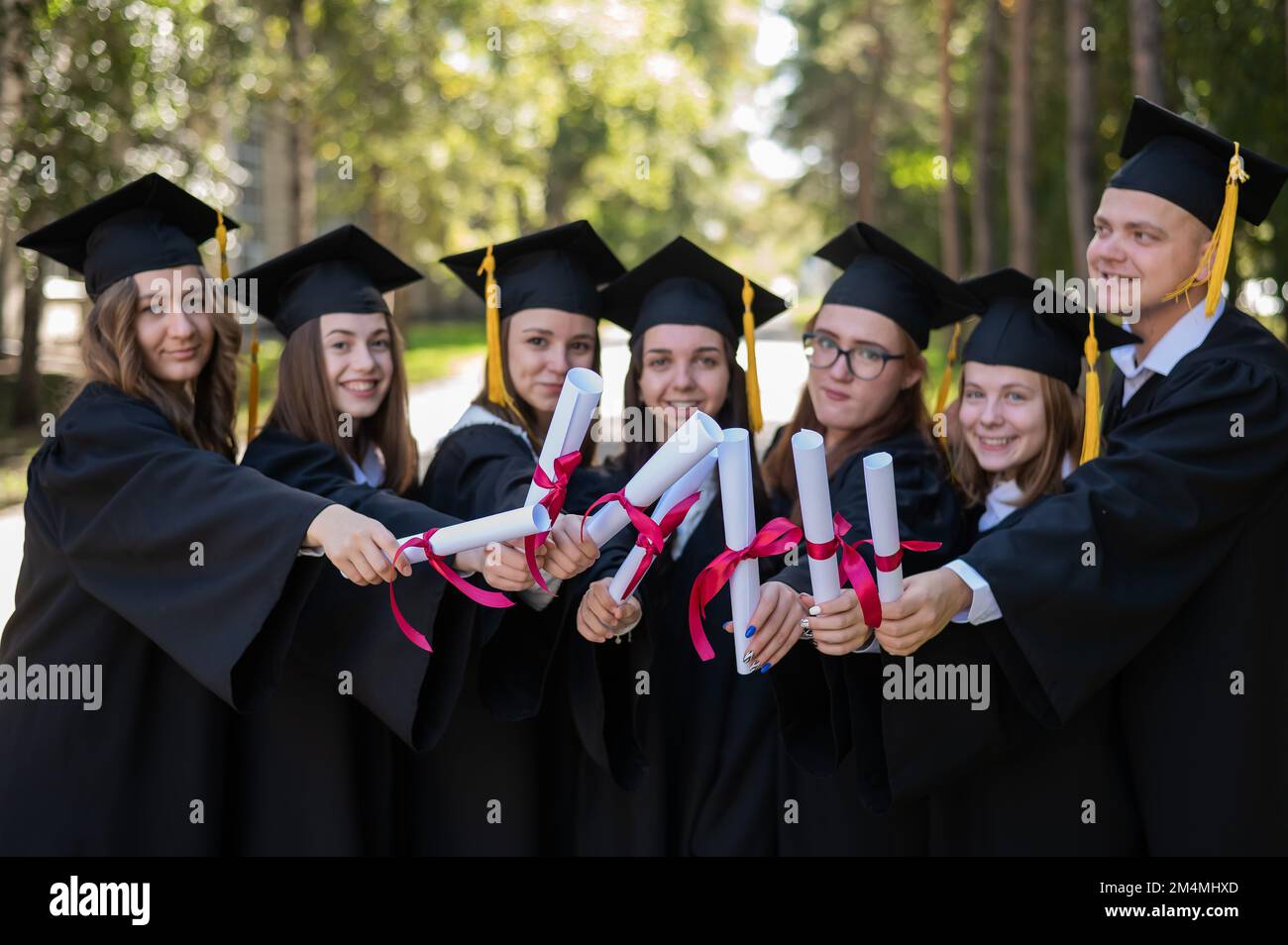 Row of happy young people in graduation gowns holding diplomas outdoors.  Stock Photo