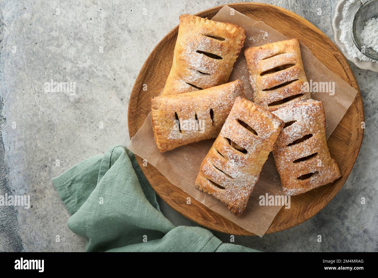 Hand pies. Mini puff pastry or hand pies stuffed with apple and sprinkle sugar powder in wooden plate. Homemade pie snack with crust for breakfast rus Stock Photo