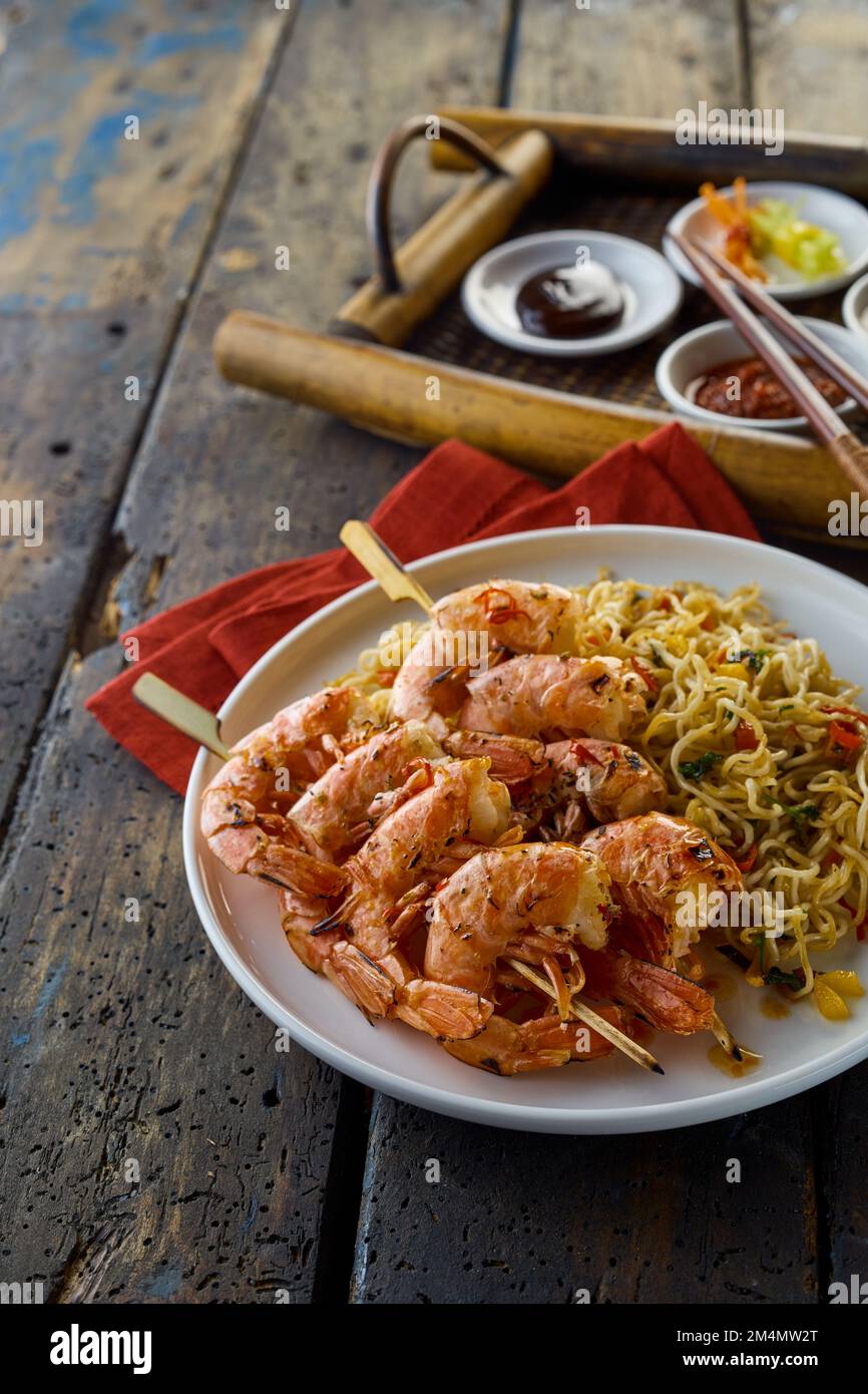 From above of appetizing Asian shrimps scampies on skewers with noodles served on wooden table with tray in light restaurant Stock Photo