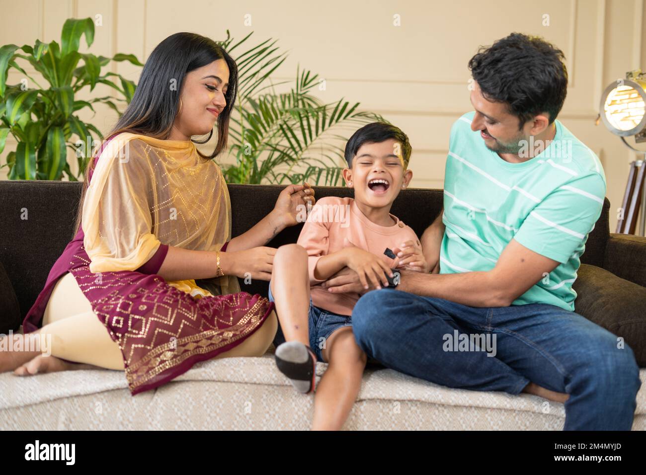 focus on mother, Happy smiling couples playing with kid by tickling or cuddling on sofa at home - concept of family bonding, affectionate and Stock Photo