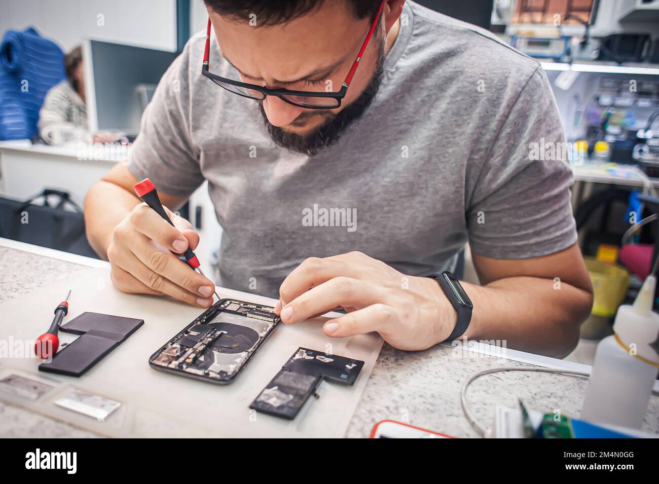 Workplace top view, close-up. Repairman disassembles smartphone with screwdriver in an electronics repair shop. Stock Photo