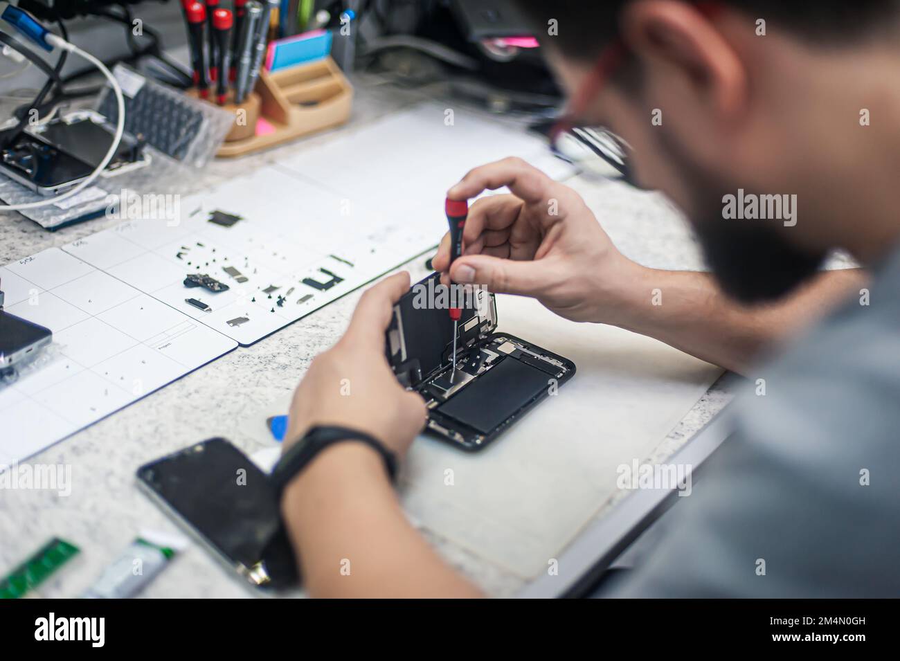 Workplace top view, close-up. Repairman disassembles smartphone with screwdriver in an electronics repair shop. Stock Photo