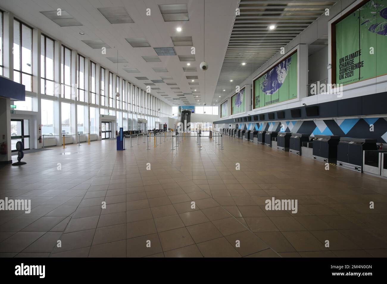Glasgow Prestwick Airport. Ayrshire Scotland. March 2022.   The deserted terminal building concourse awaiting passengers and trade. Above check in desks is  hoardings promoting COP 26 still on view Stock Photo