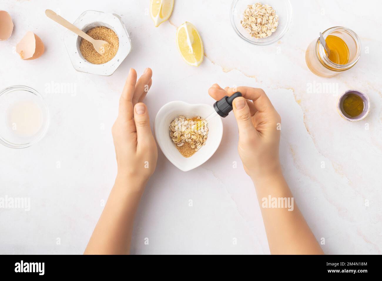 Flatlay with homemade beauty products: fresh ingredients like oat, honey, lemon, banana, egg, olive oil. Female hand holding a jar of cream. Overhead Stock Photo