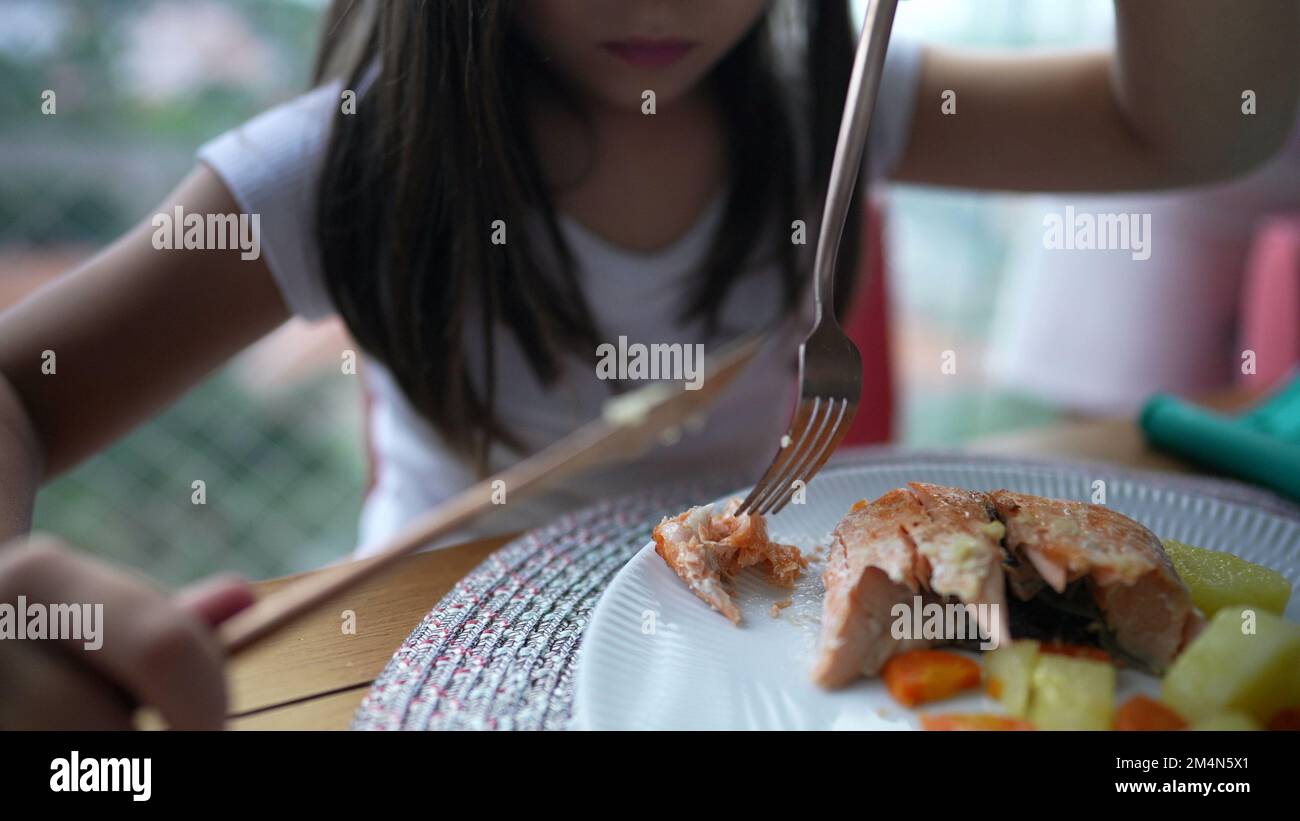 Little girl cutting piece of salmon at lunch time. Small child eating ...