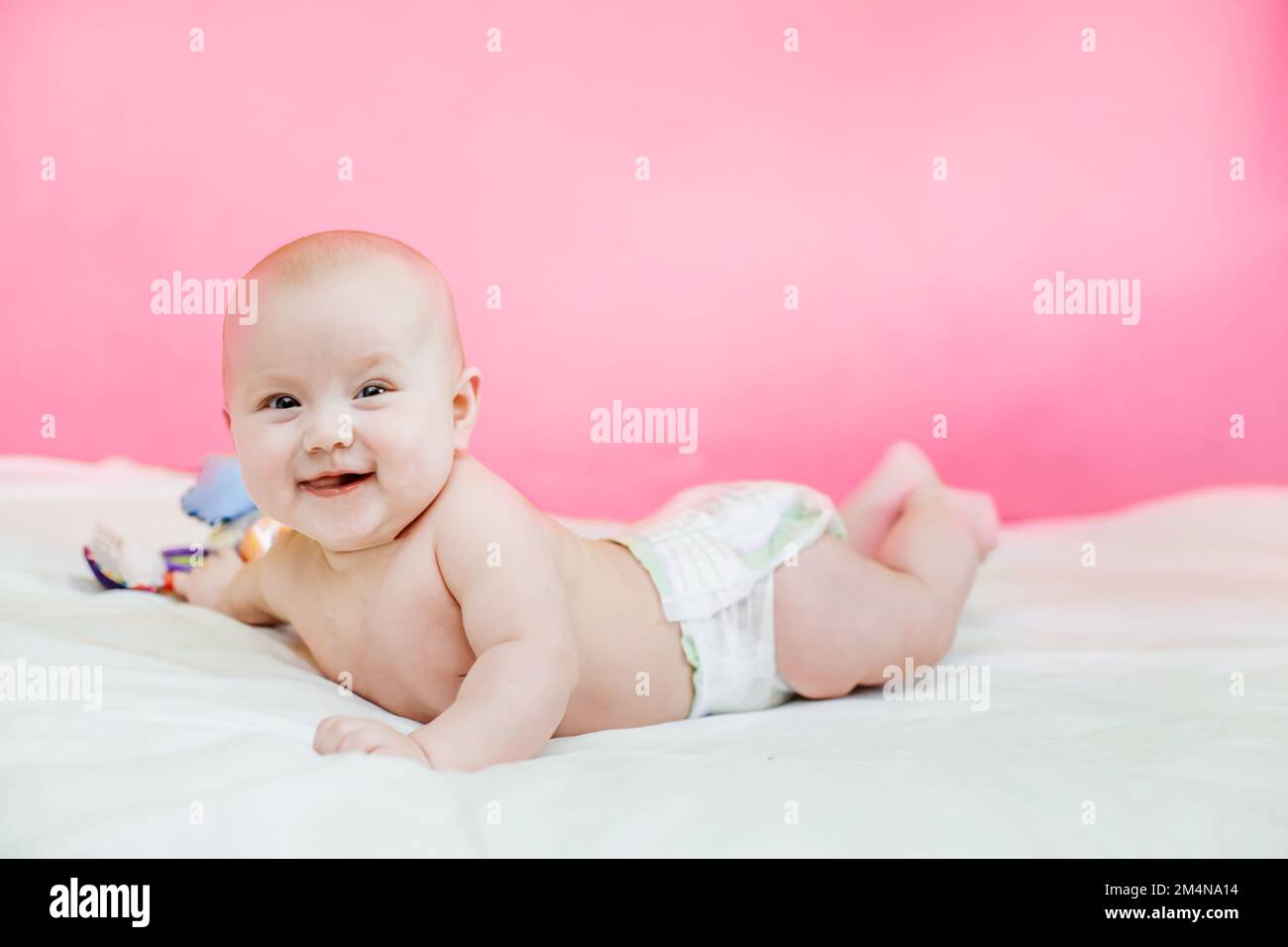 baby lies on tummy on bed with legs raised. Adorable baby boy in white