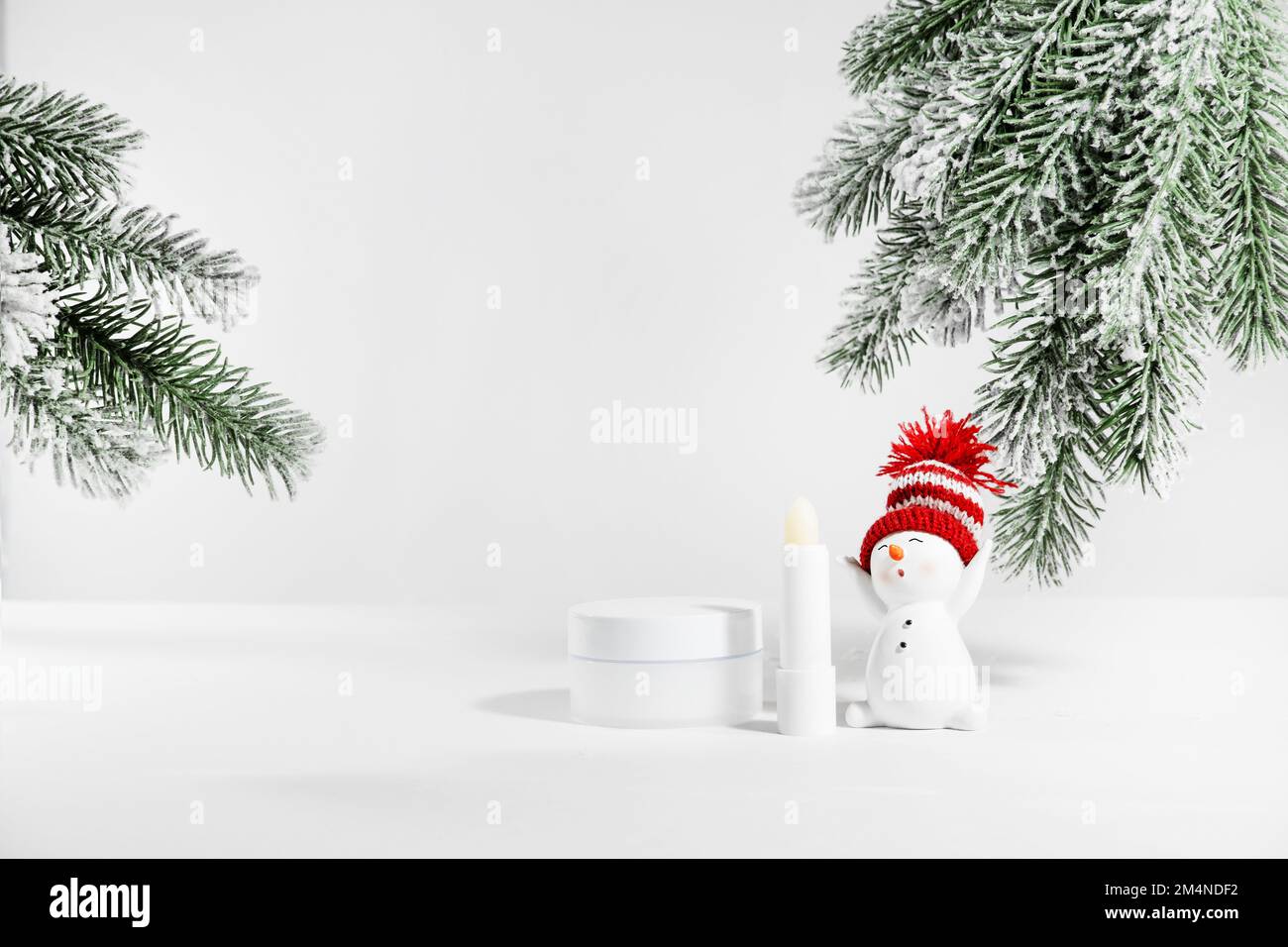 White jar of skin care cosmetics on a white surface with a snowman. Winter cosmetics. Empty container with fir branches background. Christmas gift ide Stock Photo