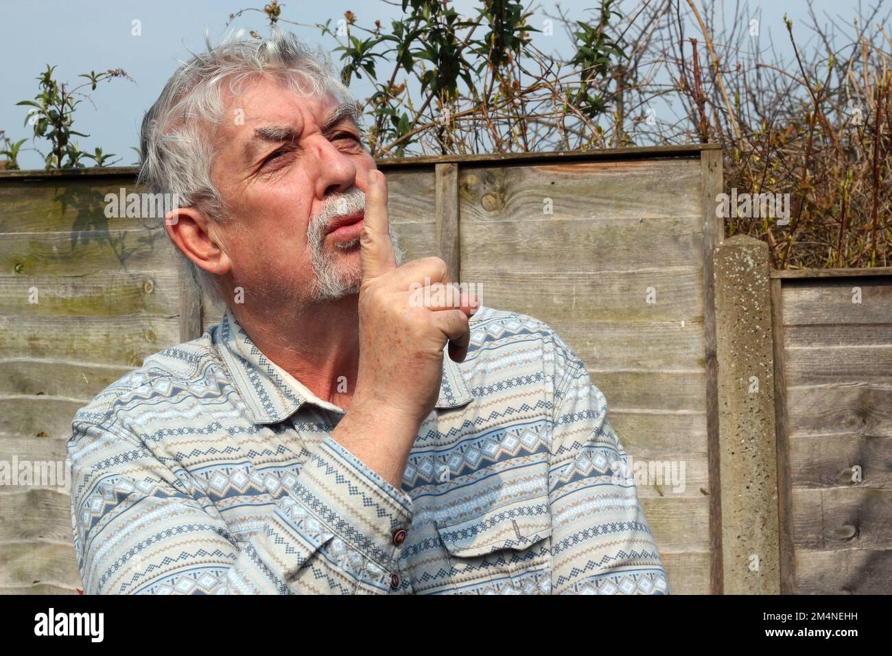 Elderly or senior man with finger to his mouth saying be quiet. Stop