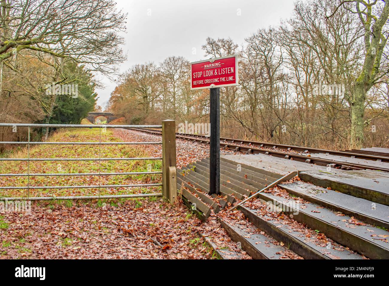 A bright red warning sign at the side of a pedestrian rail crossing at a rural track in Sussex England Stock Photo