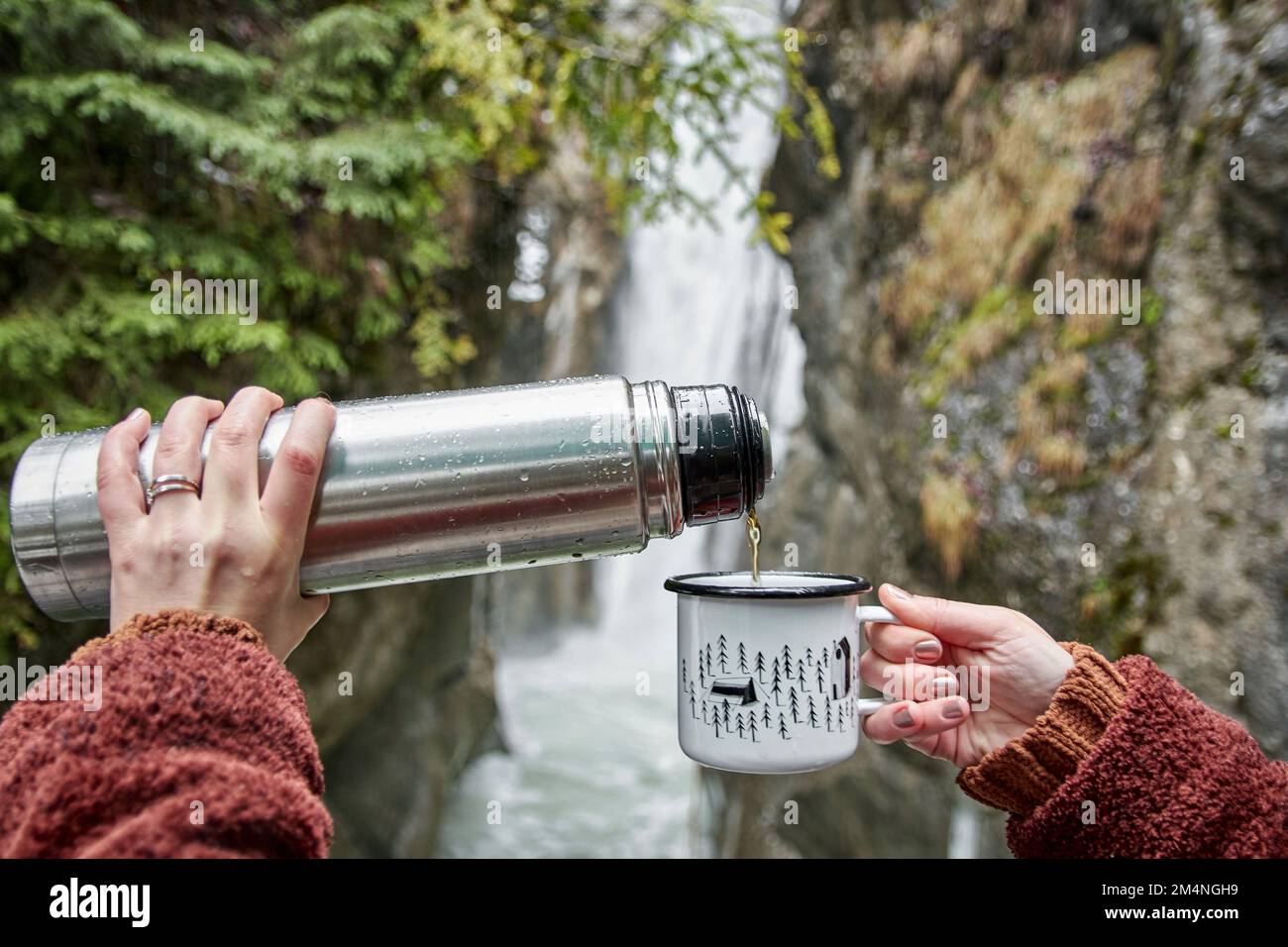 A scenic view of a woman pouring coffee into a cup while admiring the Tatzelwurm waterfall Stock Photo