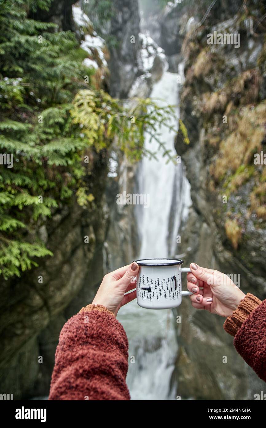 A scenic view of a woman drinking coffee while admiring the Tatzelwurm waterfall Stock Photo