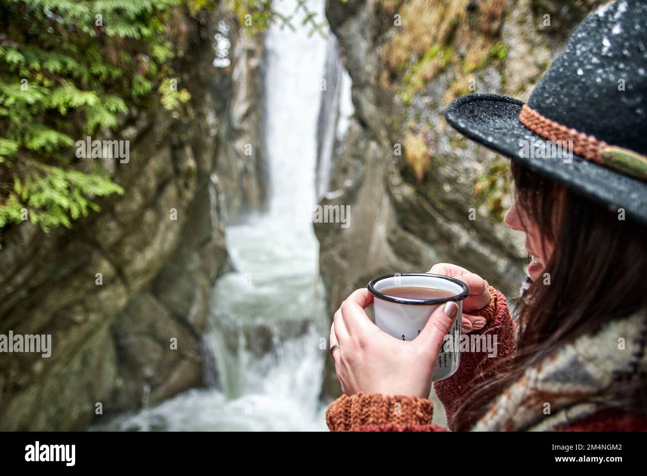 A vertical shot of a woman drinking coffee while admiring the Tatzelwurm waterfall Stock Photo
