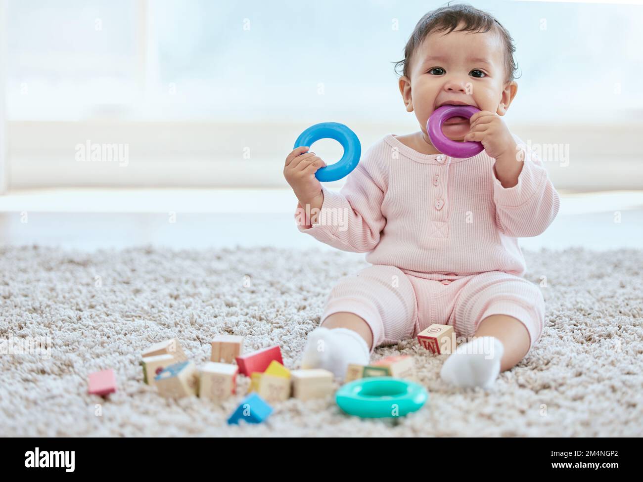 Everything goes in my mouth. an adorable baby girl sitting on the floor at home. Stock Photo