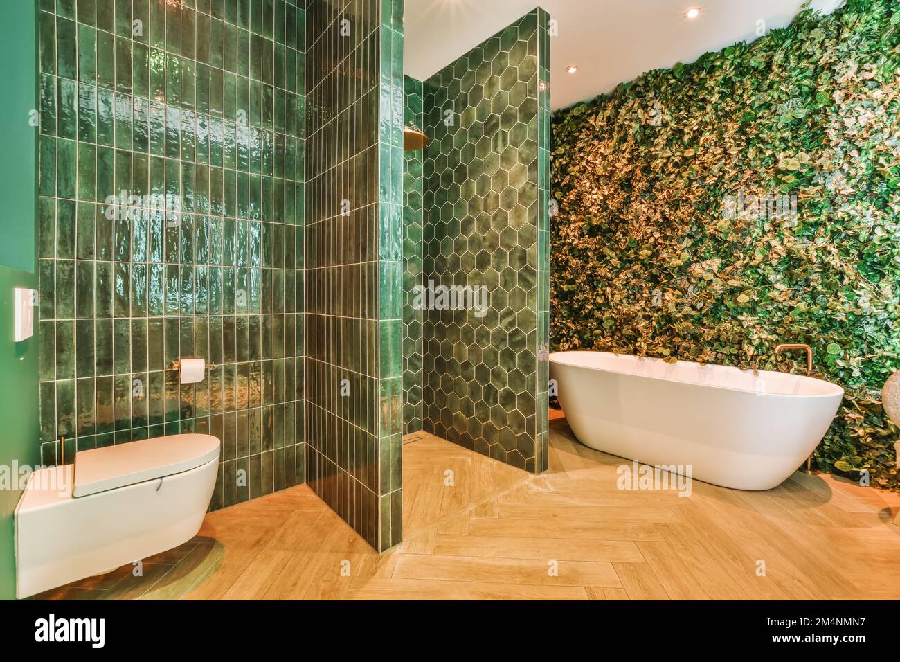 a bathroom with green tiles on the walls and wood flooring around the tub, toilet, and bathtub Stock Photo