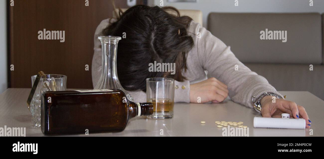 Image of a young woman passed out on the table after abusing alcohol and psychotropic drugs. Reference to the abuse and dependence of these substances Stock Photo