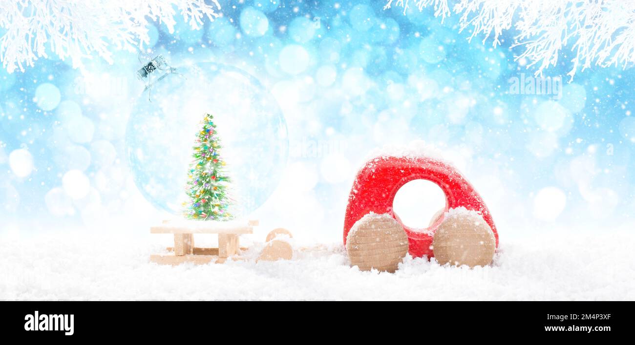 Red Wooden Car Pulling Sled with A Transparent Christmas Ball ball with green colorful glitter pine Christmas tree in perspective on bright blue bokeh Stock Photo