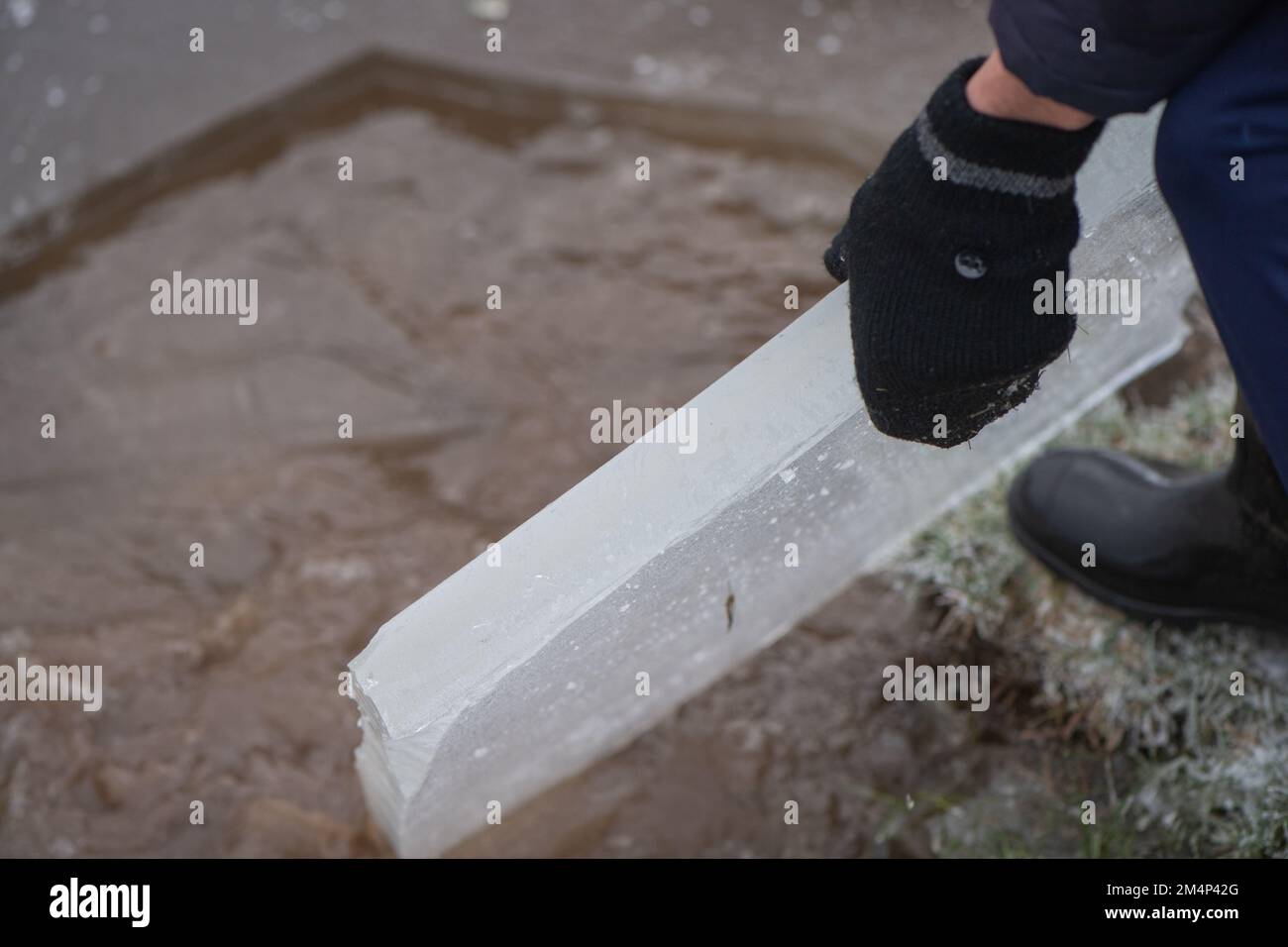 A teenage boy removes a thick piece of ice from a frozen lake during the recent cold weather in the new forest Hampshire UK. Stock Photo