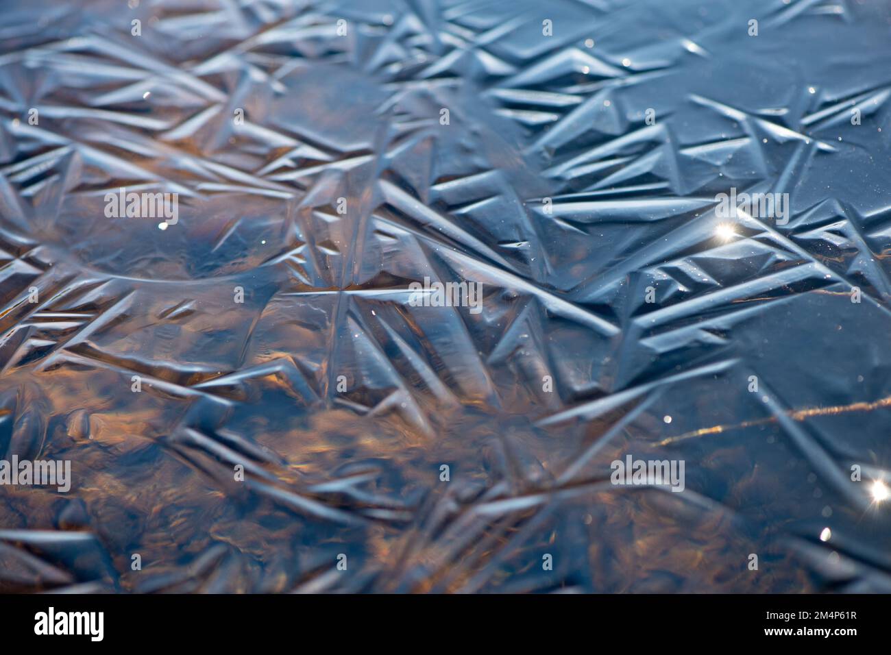 Ice patterns form on a New Forest Stream shown by catching the winter light. The stream sits within the wetlands of the national park. Stock Photo