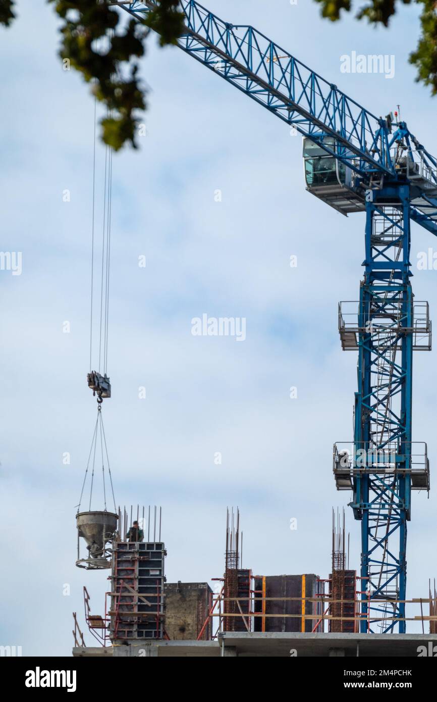 Blue tall crane with bucket of concrete on construction site with cloudy sky Stock Photo